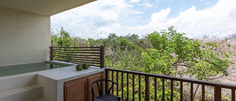 A balcony with a hot tub, wooden steps, and a chair overlooking a natural landscape.