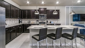 A modern kitchen with dark cabinets, a large island with bar stools, stainless steel appliances, and pendant lighting.