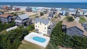 Ein Luftbild eines Küstenwohngebiets mit Häusern, einem Swimmingpool und einem Strand im Hintergrund.