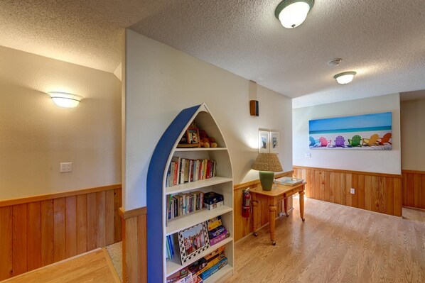 A room with a wooden floor, a bookshelf, a lamp, and a painting of beach chairs.