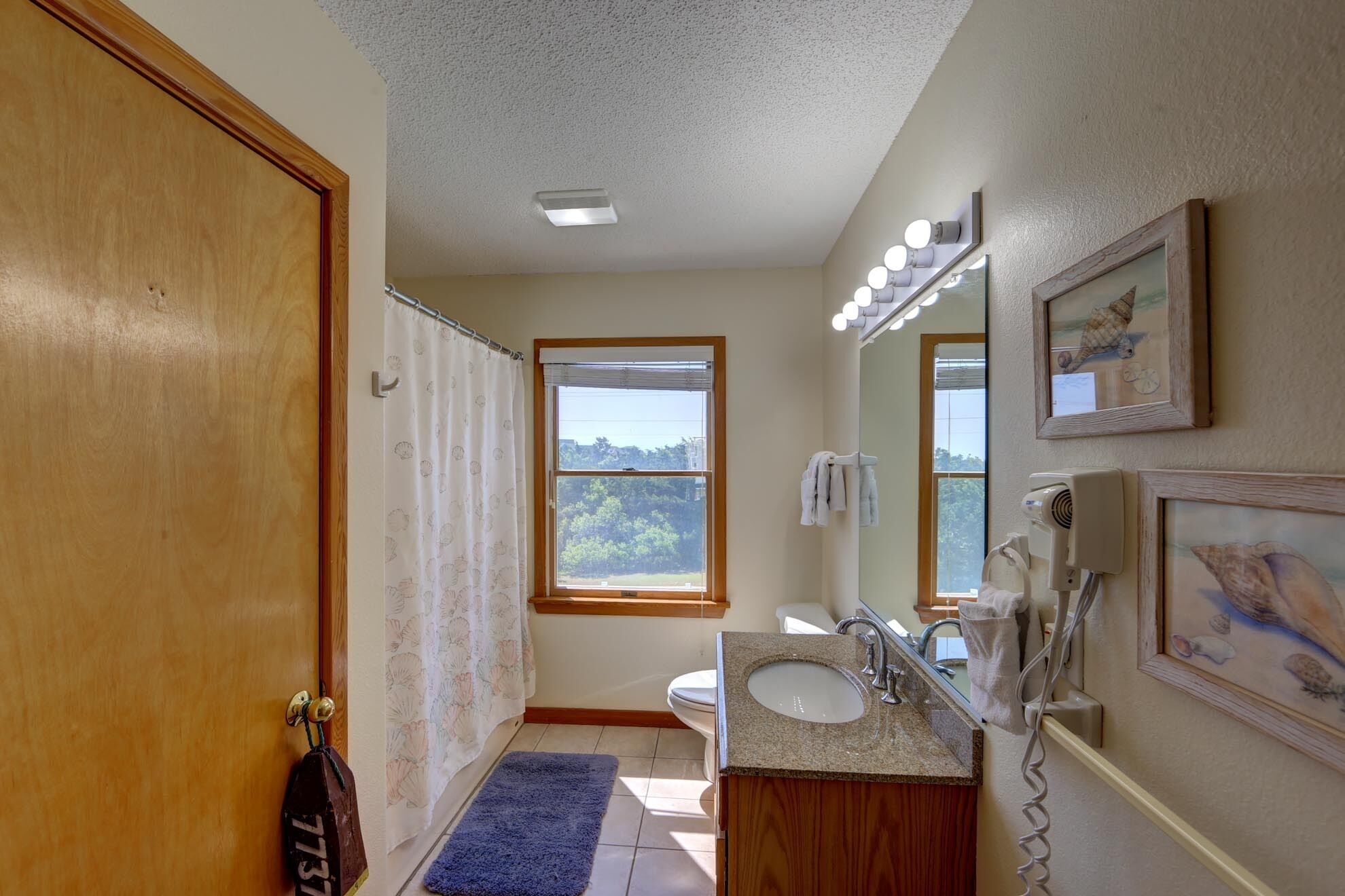A bathroom with a toilet, sink, and mirror. There is a window providing natural light and a view of greenery outside.