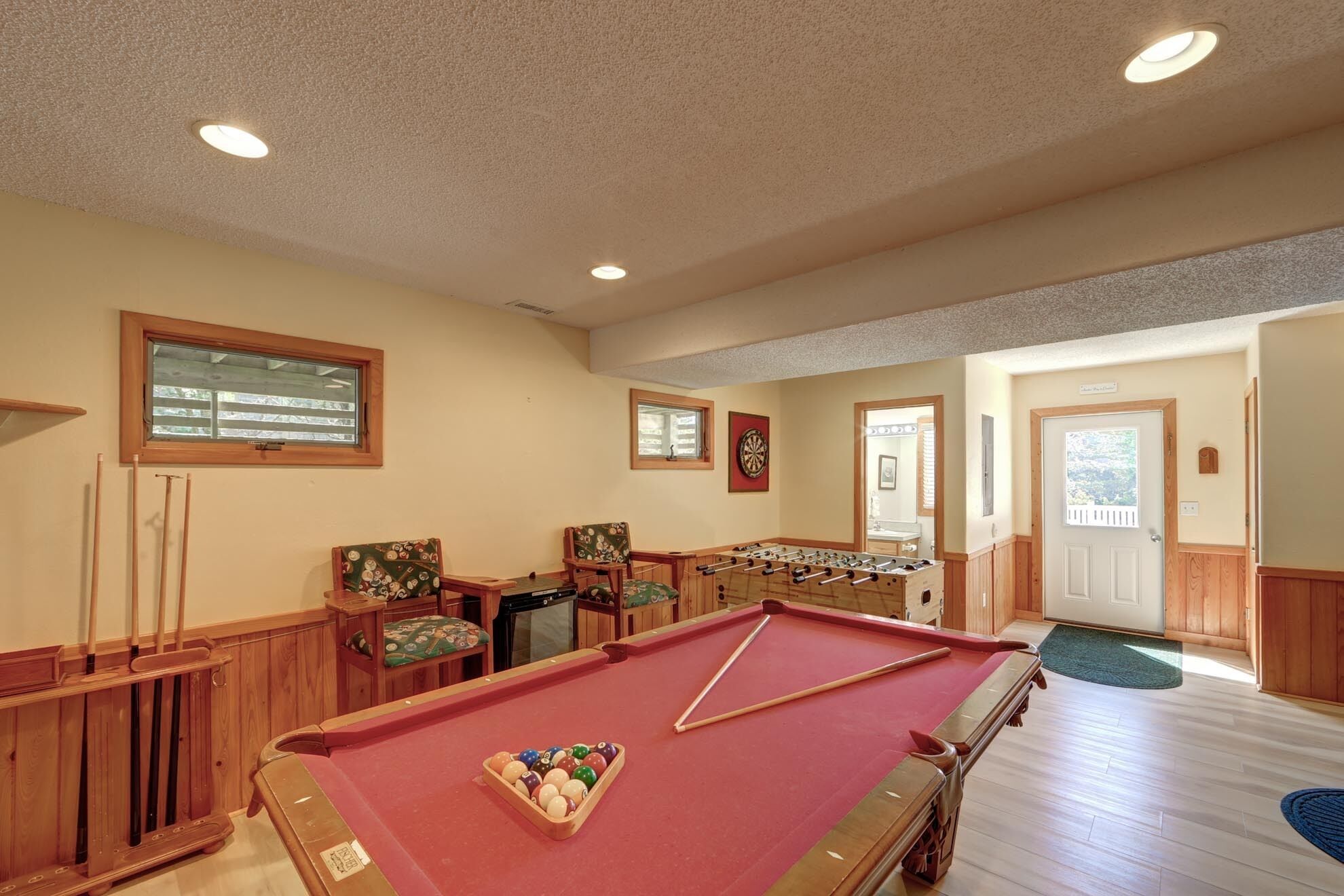 A pool table with surrounding seating and a foosball table in a room with wooden walls and ceiling.