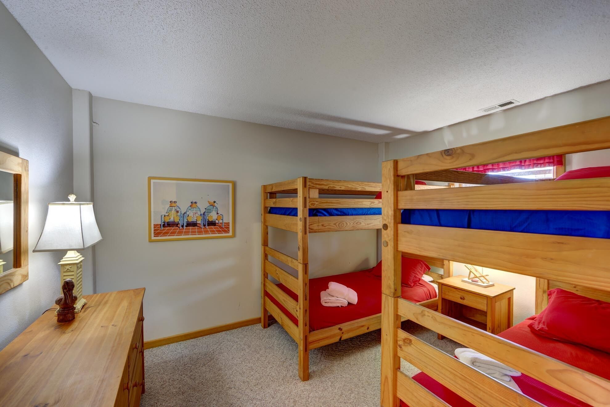 A bunk bed room with a wooden desk, a lamp, and a framed picture on the wall.