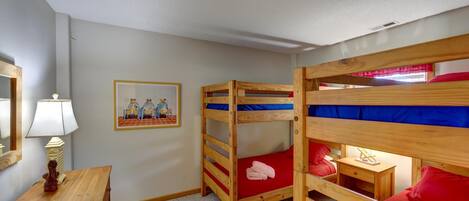 A bunk bed room with a wooden desk, a lamp, and a framed picture on the wall.