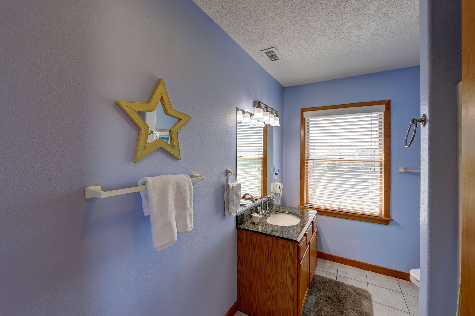 Un baño con un espejo en forma de estrella, un tocador de madera, un lavabo y una ventana con persianas.