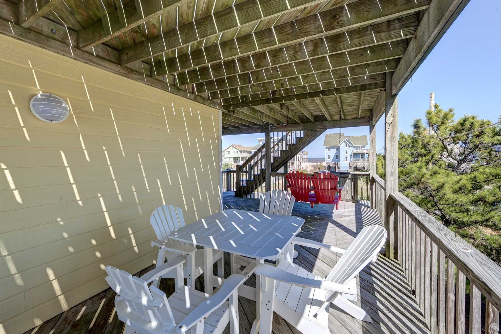 Un espacio al aire libre techado con una mesa, sillas y una escalera, con vistas a casas al fondo.