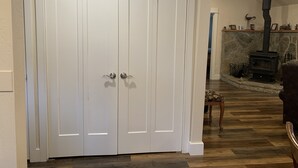 A closed white door with a handle, a stone fireplace with a chimney, and a patterned rug on the floor. - Spectacular Cozy Cottage- Wood Stove, Fire Pit, Creek (Shady Cove)