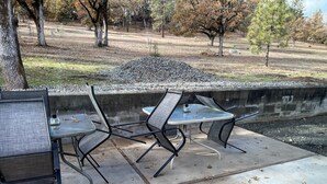 An outdoor patio with a stone wall, a table, and chairs. - Spectacular Cozy Cottage- Wood Stove, Fire Pit, Creek (Shady Cove)