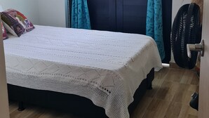 A bedroom with a bed, a window with curtains, a fan, and a door.