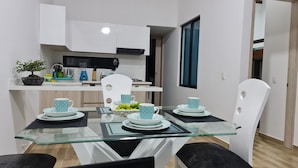 A modern kitchen with white cabinets, a black range hood, and a dining area with a glass table and white chairs.