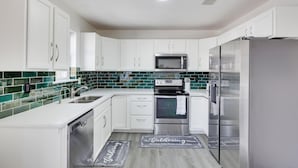 Een moderne keuken met witte kasten, roestvrijstalen apparatuur en een backsplash van groene tegels.
