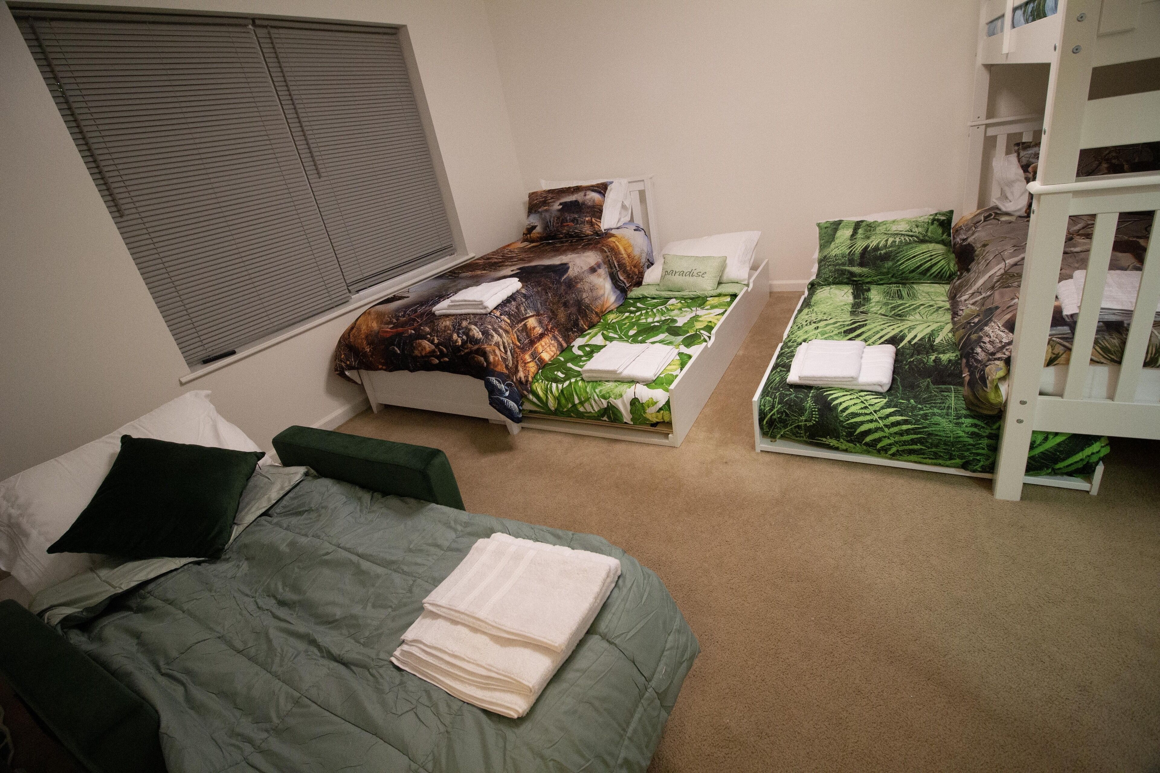 A bedroom with a bed, a green sofa, a bunk bed, and a window with blinds.