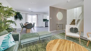 Een moderne woonkamer met een groene bank, een ronde houten salontafel, en een eethoek met een witte tafel en stoelen.