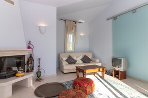 Un salon comprenant un canapé, une table basse, des poufs, une cheminée, un téléviseur et des lampes fixées au mur.
