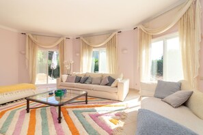 Un salon spacieux avec un canapé blanc, une table basse en verre et un tapis rayé aux couleurs vives.