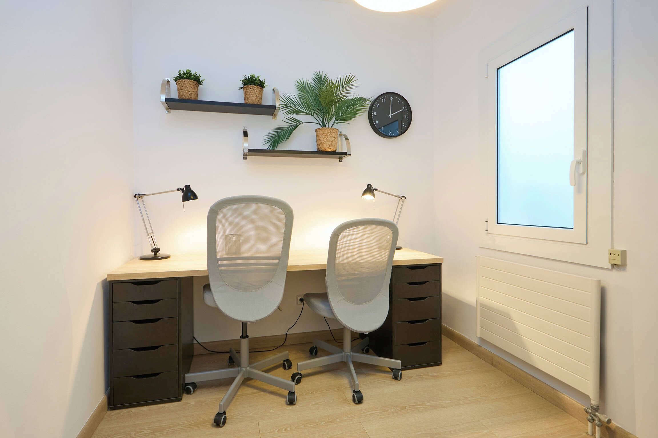 Un espace de bureau moderne comprenant un bureau, deux chaises de bureau, une horloge et des étagères avec des plantes.