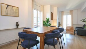 Un salon moderne avec une table à manger en bois entourée de chaises, d’un canapé et d’une grande fenêtre agrémentée de rideaux.