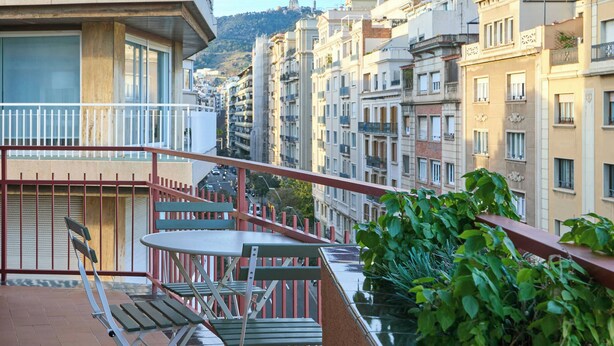 Un balcon avec une table et des chaises, donnant sur une rangée d’immeubles dotés de balcons, avec une colline en arrière-plan.