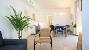 Un salon moderne avec un canapé, une table à manger et des chaises, ainsi qu’une grande plante en pot.