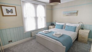 Een slaapkamer met een bed, nachtkastjes, een raam met zonwering en een wandlamp.