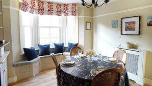 Een eetruimte met een ronde tafel voor vier personen, een erker met decoratieve gordijnen en een kroonluchter.