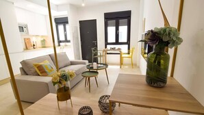 A modern living room with a sofa, coffee table, and decorative items. There is a kitchen area in the background with cabinets and a microwave. - Housing Ollerias by Sharing Co (Málaga)