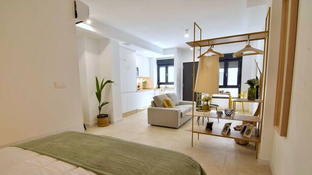 A modern bedroom with a bed, a sofa, a hanging wardrobe, and a small table with decorative items. - Housing Ollerias by Sharing Co (Málaga)