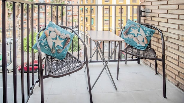 A balcony with two wicker chairs and a small table, featuring a cityscape view.