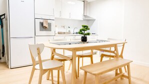 A modern kitchen with white cabinets, a built-in oven, a sink, and a dining area with a wooden table and chairs.