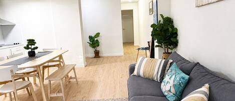 A modern living space with a dining area, a gray sofa with patterned cushions, and a potted plant.