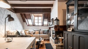 A cozy living room with a sofa, a dining table, and a kitchen area with a stove and cabinets. - Tanau 1700 (Tanau)