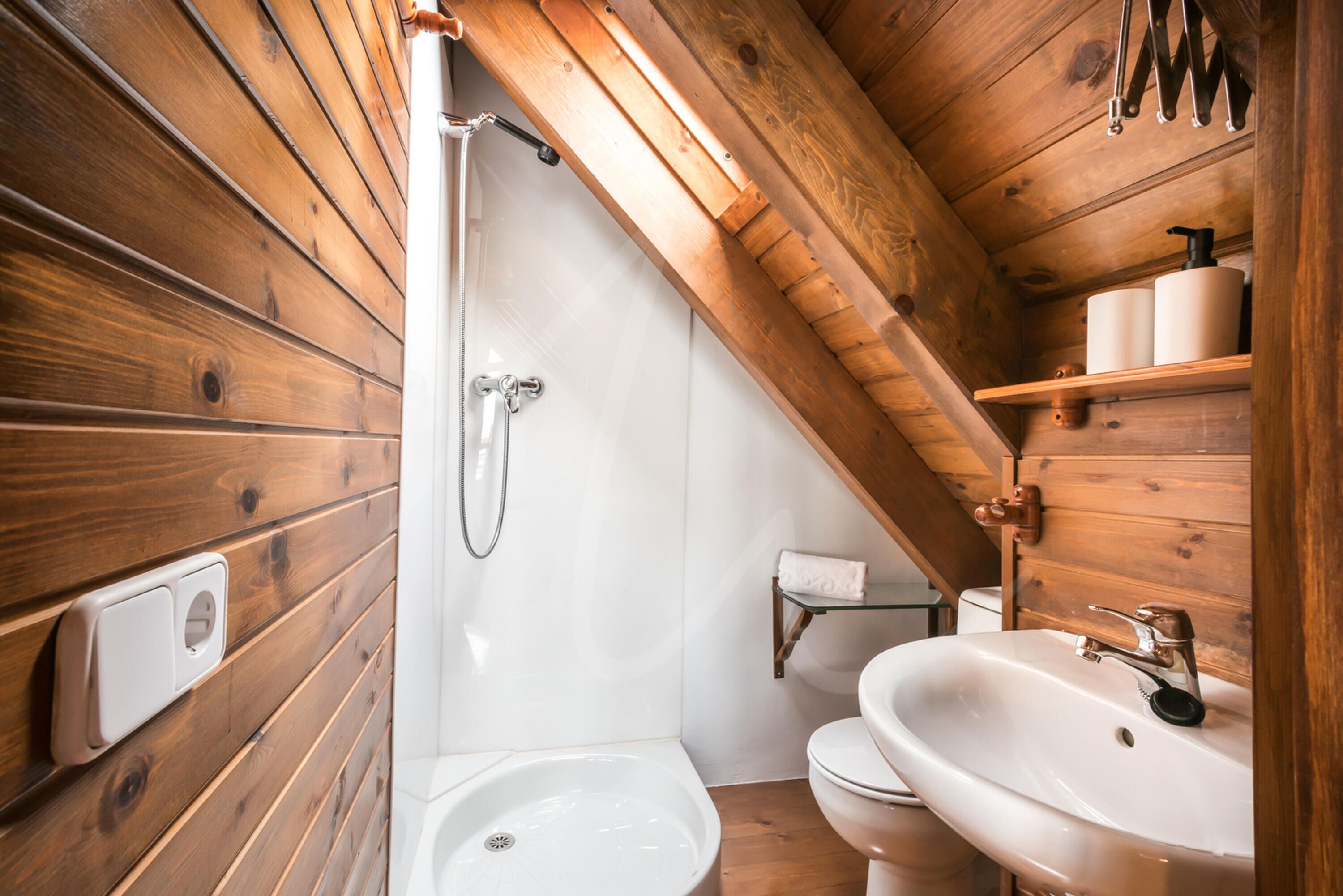 Un baño con paneles de madera, con ducha, inodoro y lavamanos.