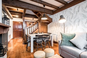 A cozy dining area with a wooden table and chairs, a staircase, and a sofa with cushions.