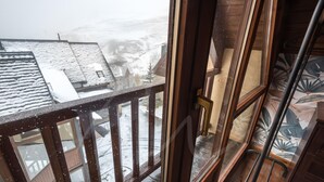 A wooden balcony with a view of a snow-covered landscape and buildings. - Tanau 1700 (Tanau)