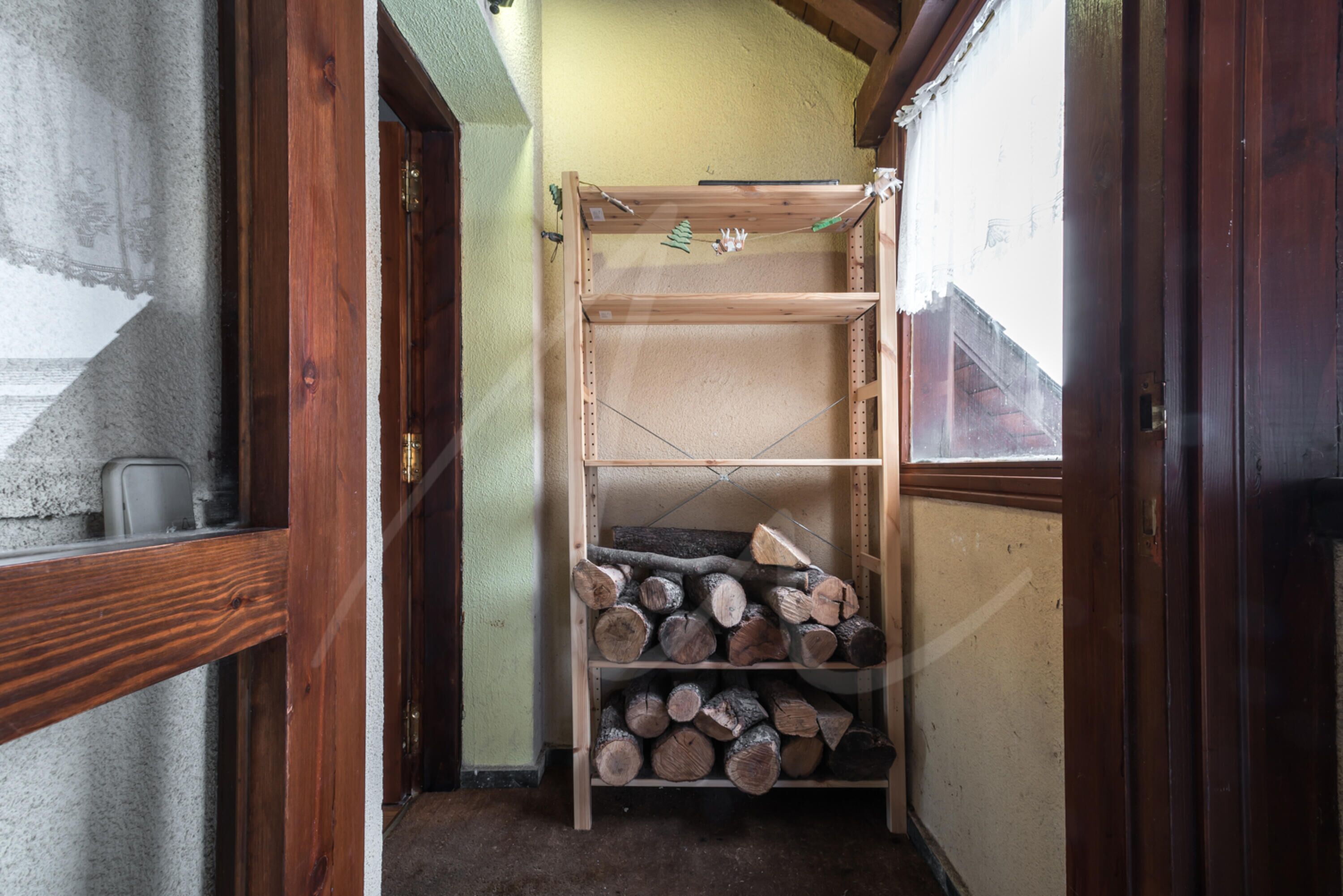A narrow hallway with a wooden shelf unit storing firewood.