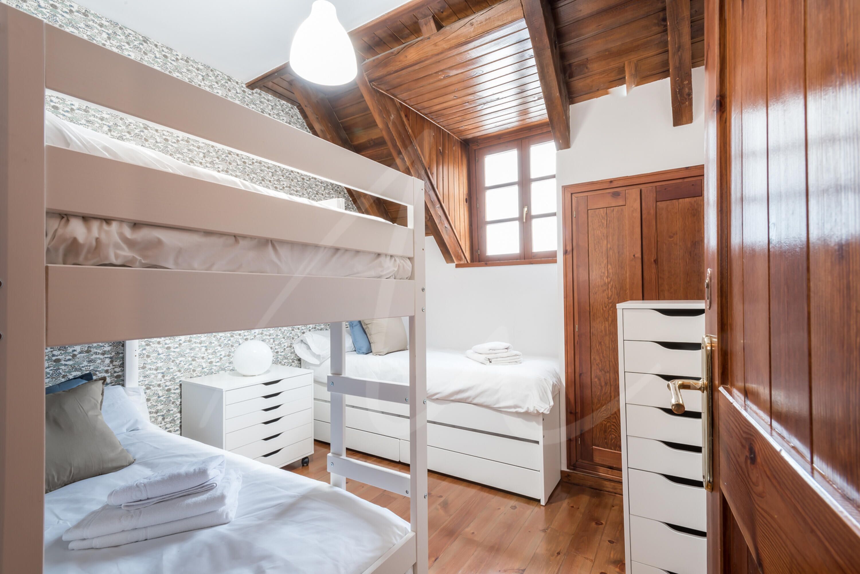 A bedroom with bunk beds, a wooden wardrobe, and a stone wall.