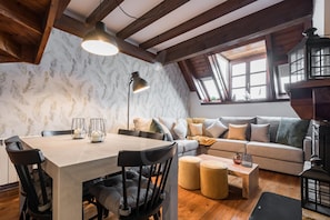 A cozy loft-style room with a dining table, chairs, a sofa, and a wooden ceiling.