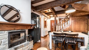 A cozy interior with a stone fireplace, wooden beams, a dining area with chairs, and a staircase. - Tanau 1700 (Tanau)