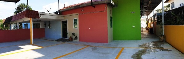 A parking area with marked spaces, a covered entrance, and a building with a red and green facade.