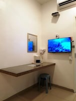 Una habitación pequeña y limpia con un mostrador de madera, un espejo, un televisor, un teléfono y un taburete.