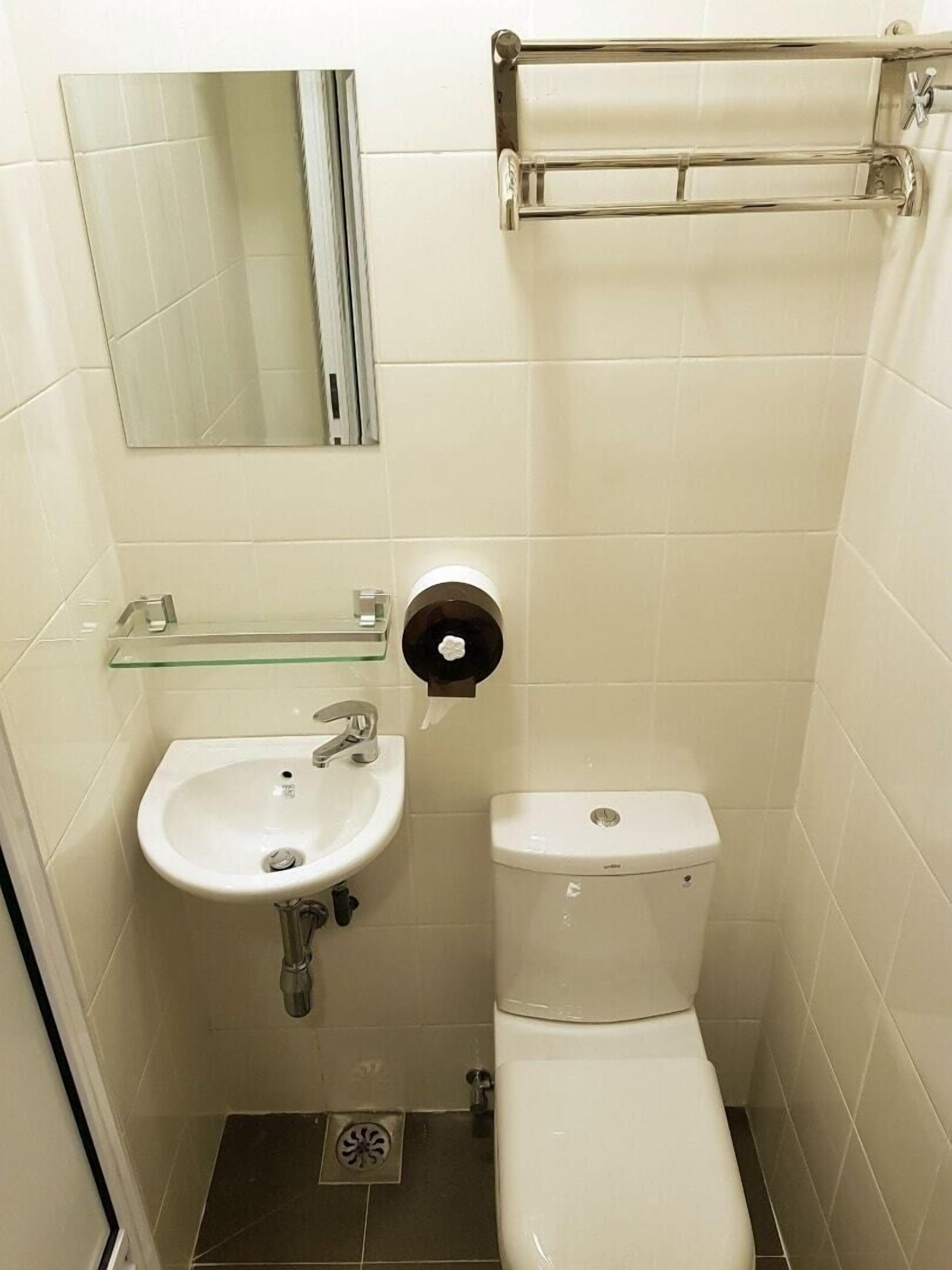 Un baño pequeño y funcional con un lavamanos blanco, inodoro y estante de vidrio sobre el lavamanos.