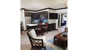 A modern kitchen with dark cabinets, stainless steel appliances, and a blue tiled backsplash. There is a dining area with a wooden table and chairs.