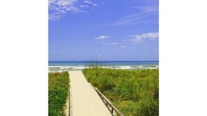 A beach path with a wooden railing, leading to the ocean.