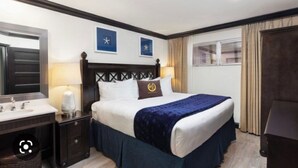 A hotel room with a bed, two bedside tables, a nightstand, a mirror, and a window with curtains.