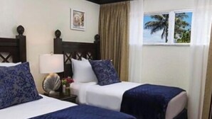 A hotel room with two beds, each with a blue bedspread and white linens. There is a nightstand with a lamp and a picture frame on the wall.