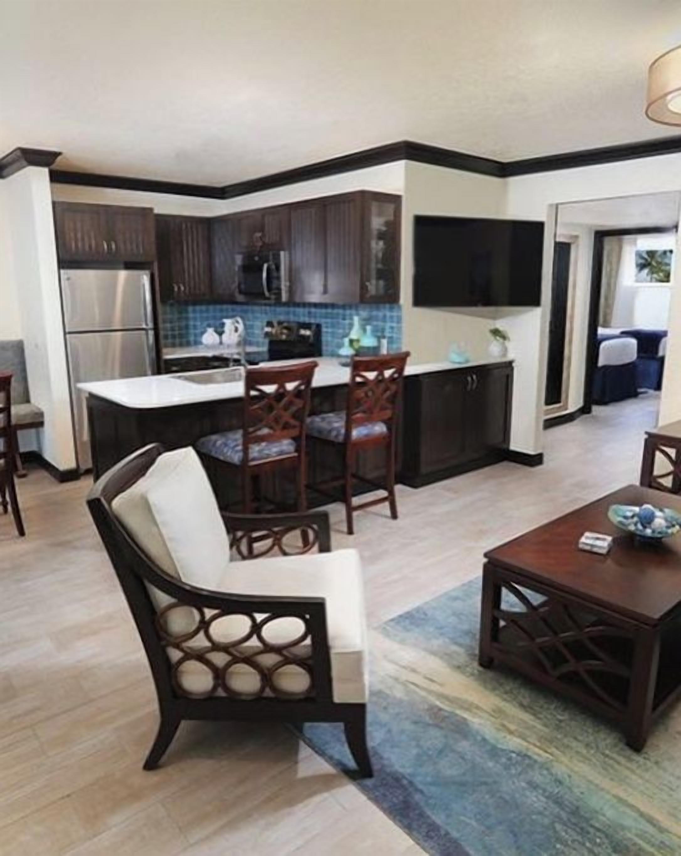 A modern kitchen with dark cabinets, stainless steel appliances, and a blue tiled backsplash. There is a dining area with a wooden table and chairs.