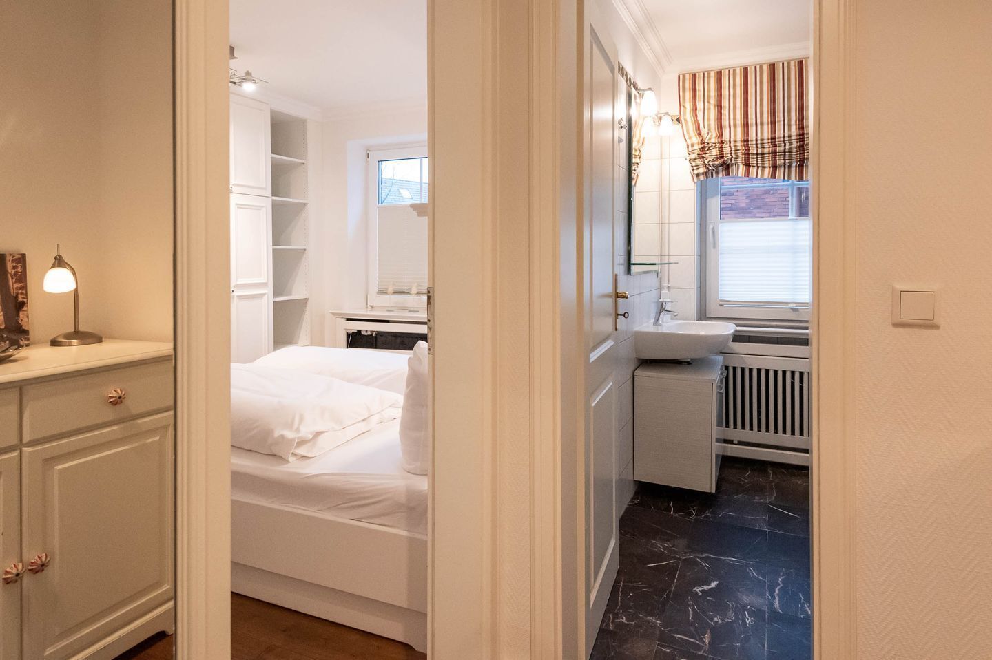 Une chambre à coucher comprenant un lit, une table de chevet avec une lampe, une armoire et une salle de bain avec un lavabo et une fenêtre.