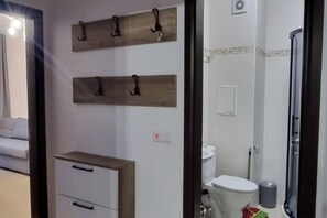 A bathroom with a toilet, a shower, and a sink. There are wooden shelves with hooks above the toilet.