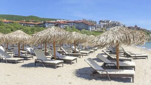 A beach with rows of sun loungers and thatched umbrellas, a clear sky, and buildings in the background. - Apartment Sleeps 4 with Pools Access - Smart TVs (Sunny beach)