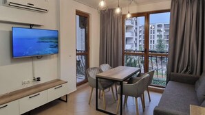 A modern living room with a flat-screen TV, dining table, chairs, and a sofa. - Apartment Sleeps 4 with Pools Access - Smart TVs (Sunny beach)